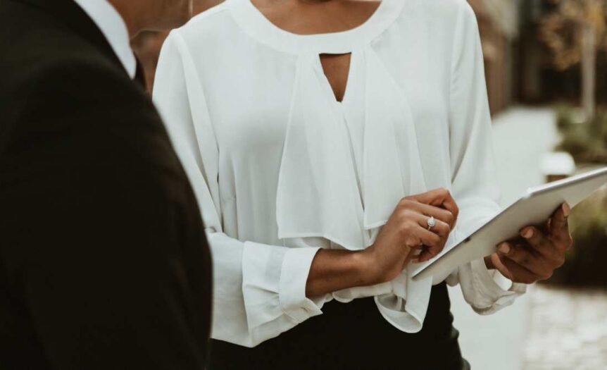 A woman, who has a wedding ring on their left finger, is using digital device to show something to someone.