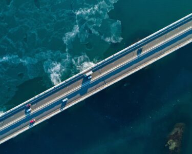 Cars crossing a highway that spans a large body of water. Small waves are happening under the highway.