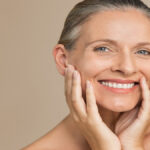 An older woman model is showing off her perfect, glowing skin with her hair slicked back into a bun.