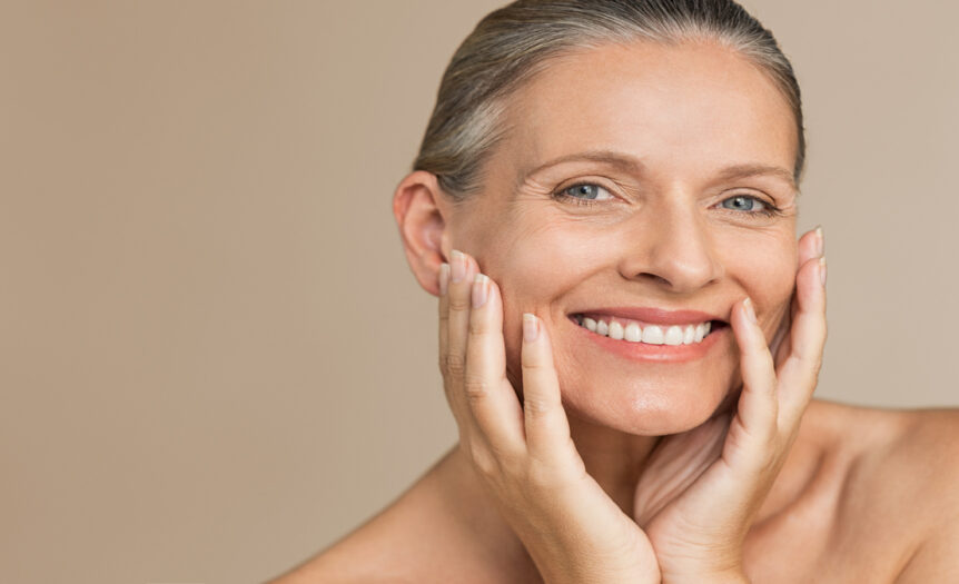 An older woman model is showing off her perfect, glowing skin with her hair slicked back into a bun.