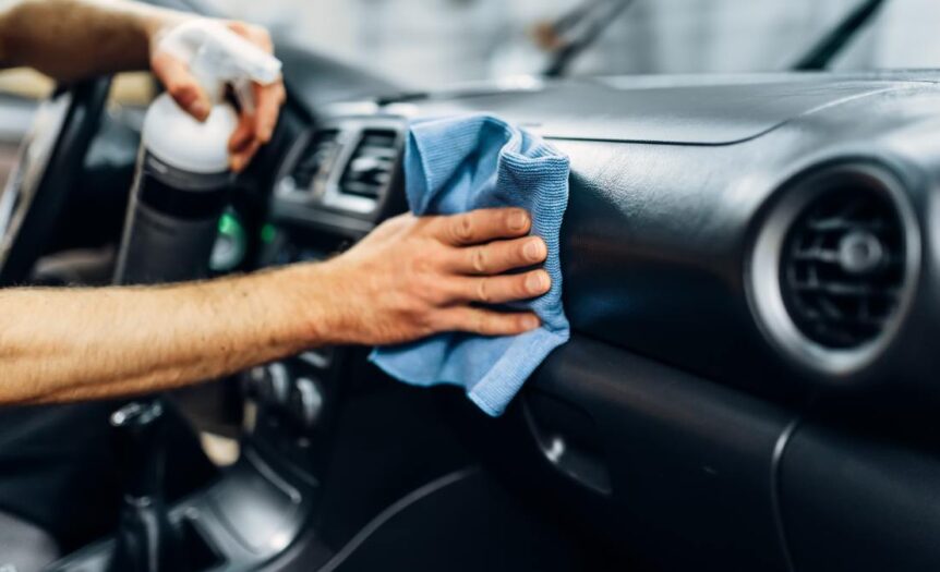 A close-up of someone's hands as they detail and clean the car's leather interior with polishing spray.