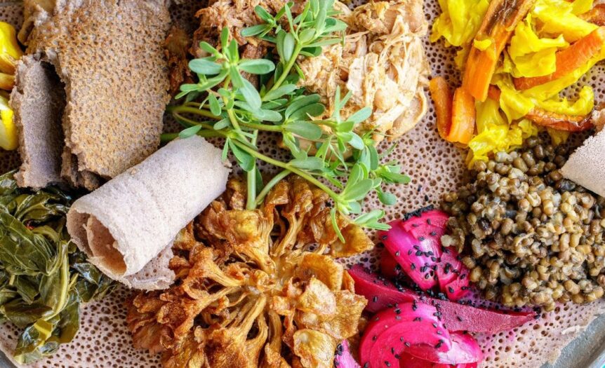 A close-up on a plate of Ethiopian food. There are different meats, vegetables, and grains on top of an injera flatbread.