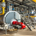 An industrial boiler room with three large boilers inside. There are metal stairs to maintain the boilers.