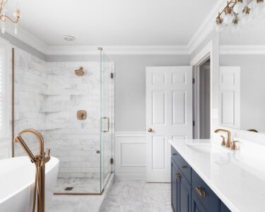 A large, modern bathroom with a standalone tub, a chandelier, a shower, and a long vanity with blue cabinets.