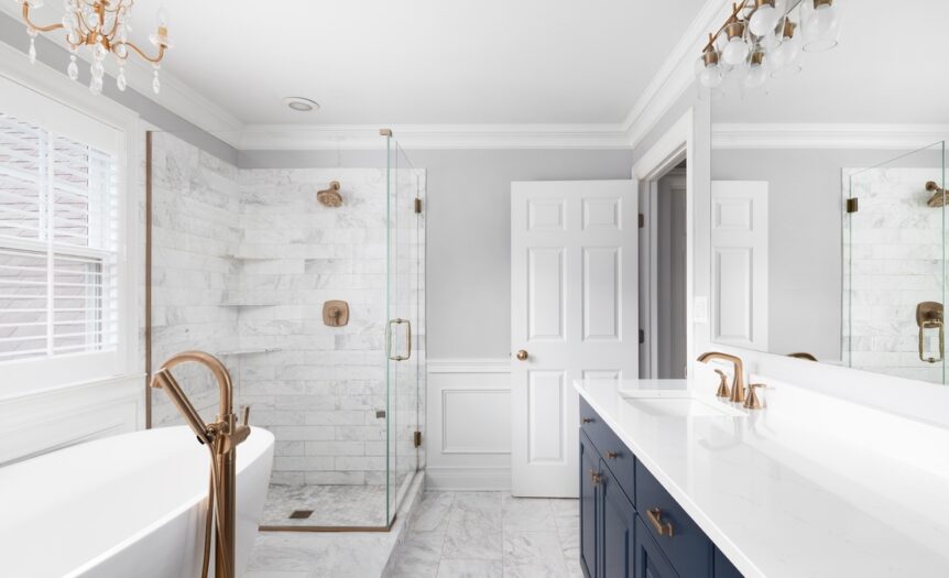 A large, modern bathroom with a standalone tub, a chandelier, a shower, and a long vanity with blue cabinets.