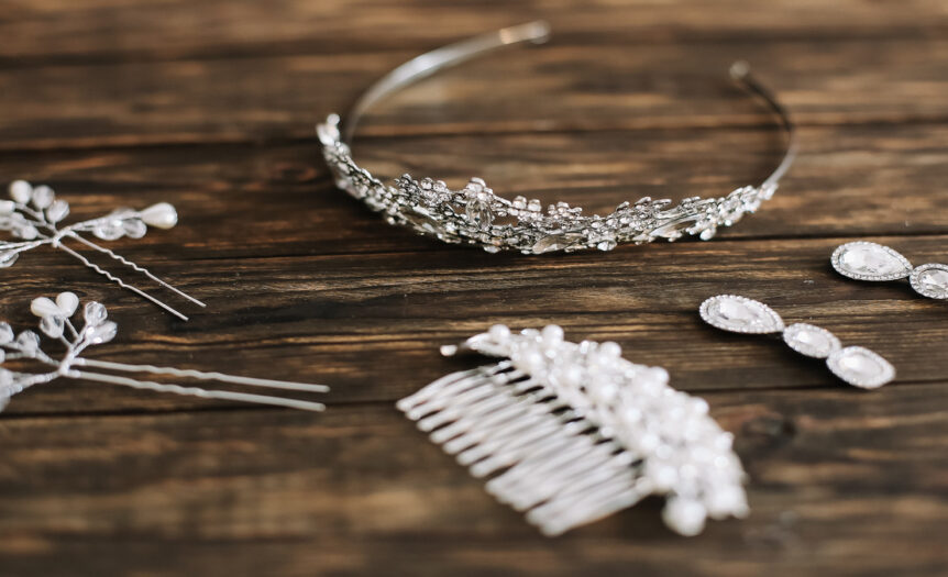 A pair of sparkly earrings, decorative hair pins, a hair comb, and a tiara, laid out on a dark wood surface.