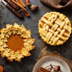 Three pumpkin pies surrounded by an assortment of decorative items, including cinnamon sticks, acorns, and mini pumpkins.