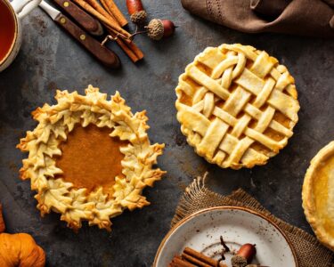 Three pumpkin pies surrounded by an assortment of decorative items, including cinnamon sticks, acorns, and mini pumpkins.