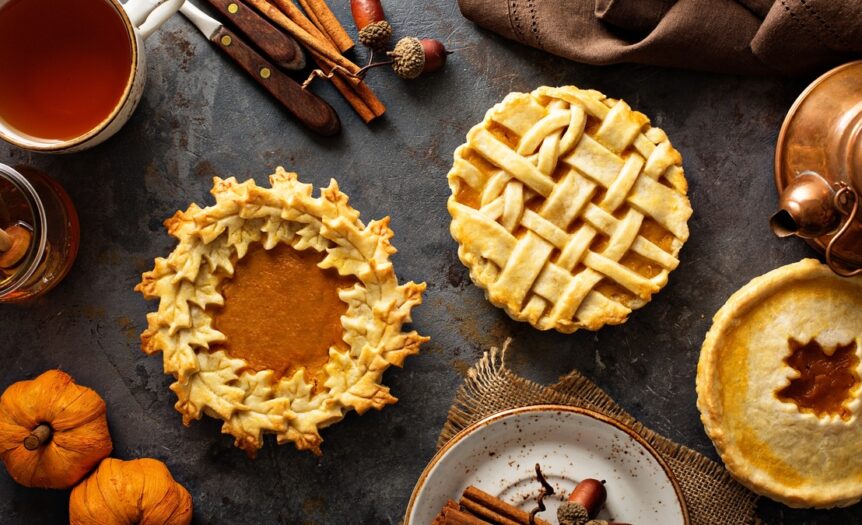 Three pumpkin pies surrounded by an assortment of decorative items, including cinnamon sticks, acorns, and mini pumpkins.
