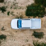 An overhead view of a white truck off-roading through a desert landscape. There are green bushes growing nearby.