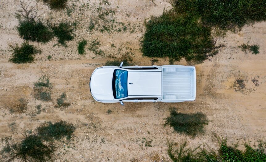 An overhead view of a white truck off-roading through a desert landscape. There are green bushes growing nearby.
