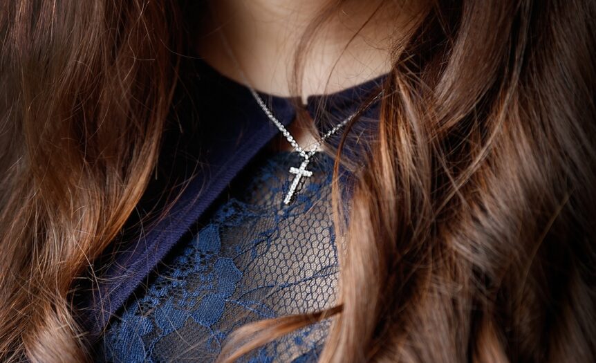 A close-up view shows a person wearing a blue, lacy top and a silver cross necklace on a silver chain.