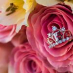 A pink rose bouquet with a silver "15" ring adorned with gemstones in the center; other roses and lilies surround it.