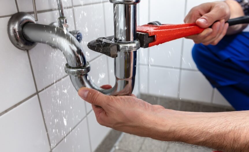 A person's hands are working to fix a leaking pipe. They have one hand on the pipe and the other holding a wrench.