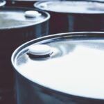 A close-up view shows six black barrels with silver tops and white plugs sitting in two rows of three.