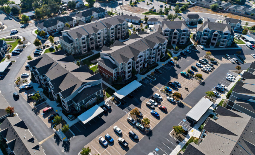 An aerial view of several residential apartment complexes. The parking lot is full of parked cars.