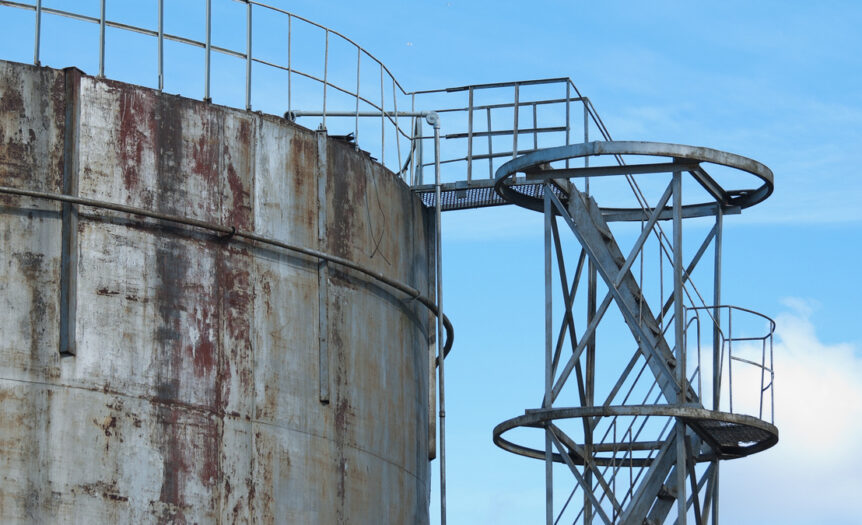 A side staircase leading up to an old, metal water container tank with rust marks against a blue sky.