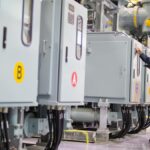 An employee in an industrial facility is holding a tablet and using a pen to place a mark on a machine.