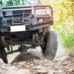 A truck is driving up a dirt road. On either side of the road is greenery like trees and grass.