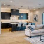 An open concept family home with a living room next to the kitchen space, separated by bar stools and a sofa.