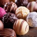 A close-up view shows various types of specialty chocolate spheres placed in several organized lines.