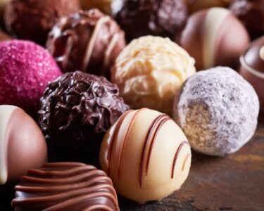 A close-up view shows various types of specialty chocolate spheres placed in several organized lines.