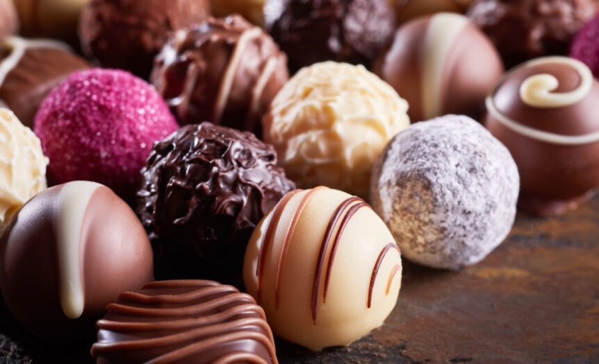 A close-up view shows various types of specialty chocolate spheres placed in several organized lines.