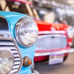 Close up of colorful vintage cars lined up indoors, highlighting classic design details and shiny chrome in a garage setting.