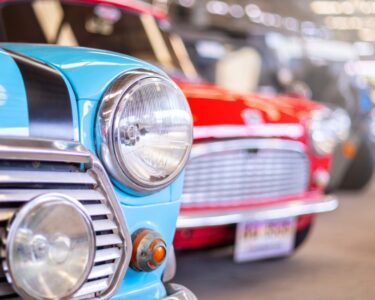 Close up of colorful vintage cars lined up indoors, highlighting classic design details and shiny chrome in a garage setting.
