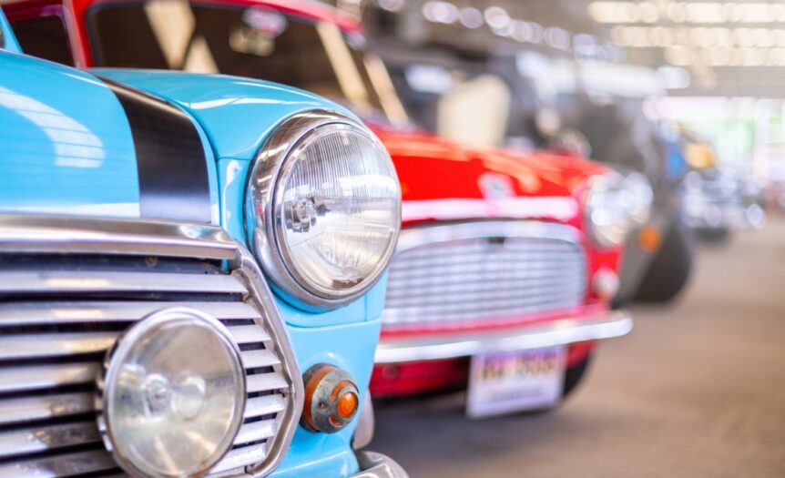 Close up of colorful vintage cars lined up indoors, highlighting classic design details and shiny chrome in a garage setting.