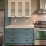 A kitchen with green cabinets, black hardware, stainless steel appliances, and a beige tiled backsplash.