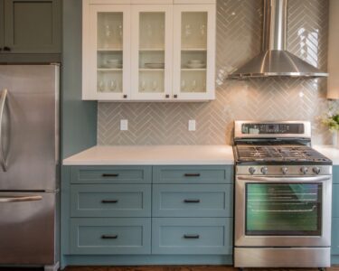 A kitchen with green cabinets, black hardware, stainless steel appliances, and a beige tiled backsplash.