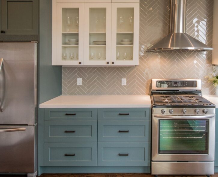 A kitchen with green cabinets, black hardware, stainless steel appliances, and a beige tiled backsplash.