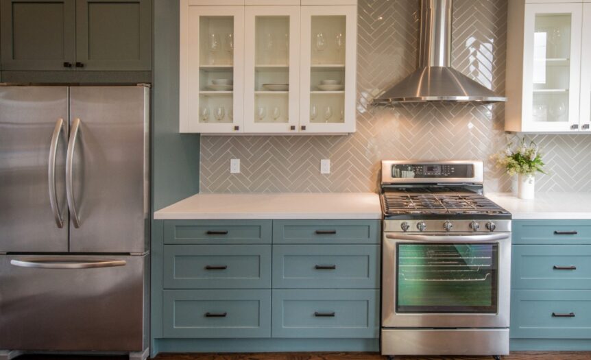 A kitchen with green cabinets, black hardware, stainless steel appliances, and a beige tiled backsplash.