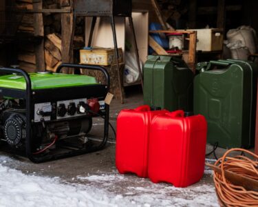 A green portable gas generator on a snowy driveway in front of an open garage stall next to two red gas cannisters.