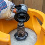 A close-up view shows a person wearing a gray glove placing a gas regulator on a gas cylinder that sits outside.