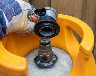 A close-up view shows a person wearing a gray glove placing a gas regulator on a gas cylinder that sits outside.