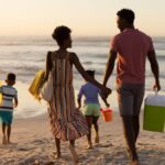 A school-aged son and daughter run on a beach in front of their mom and dad who are holding hands behind them.