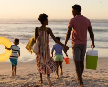 A school-aged son and daughter run on a beach in front of their mom and dad who are holding hands behind them.