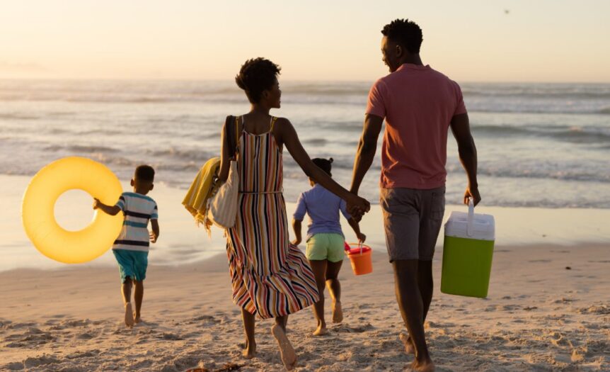 A school-aged son and daughter run on a beach in front of their mom and dad who are holding hands behind them.