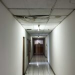 A poorly lit hallway with dilapidated ceiling tiles. The tiles are water stained and falling down into the hallway.