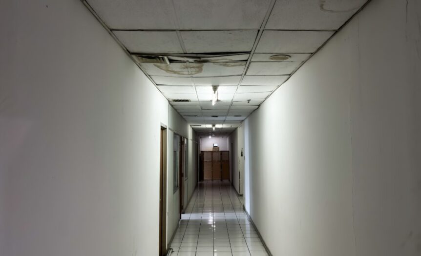 A poorly lit hallway with dilapidated ceiling tiles. The tiles are water stained and falling down into the hallway.