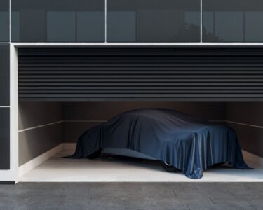 A car inside of a modern looking garage with a tarp over the top of it. A single camera points out from the garage wall.