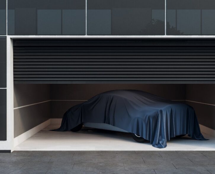 A car inside of a modern looking garage with a tarp over the top of it. A single camera points out from the garage wall.